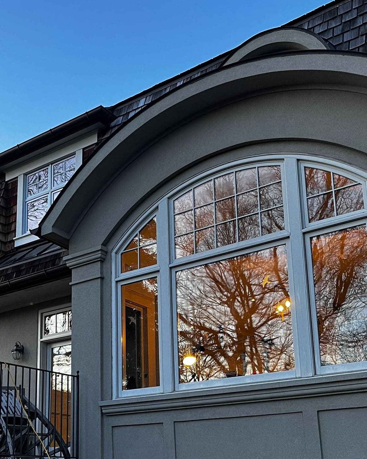 A home’s arched front window at dusk, cleaned inside and out, reflecting the trees across the street